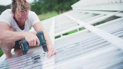 a man screwing transparent polycarbonate roof sheet using electric screw driver