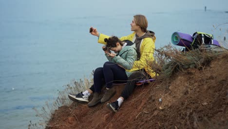Traveler-couple-sitting-on-top-of-the-cliff-and-posing-taking-selfie-using-smartphone