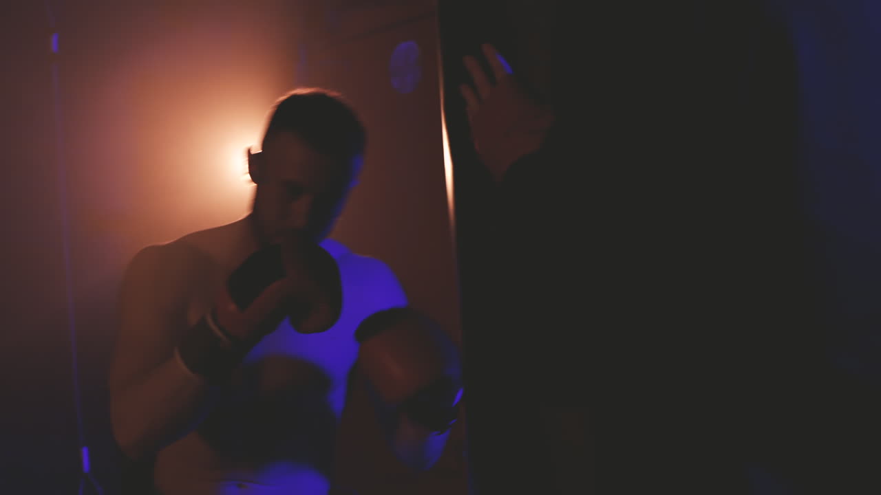 셔츠를 입지 않은 권투 선수가 복싱 백을 펀칭하여 워밍업 1