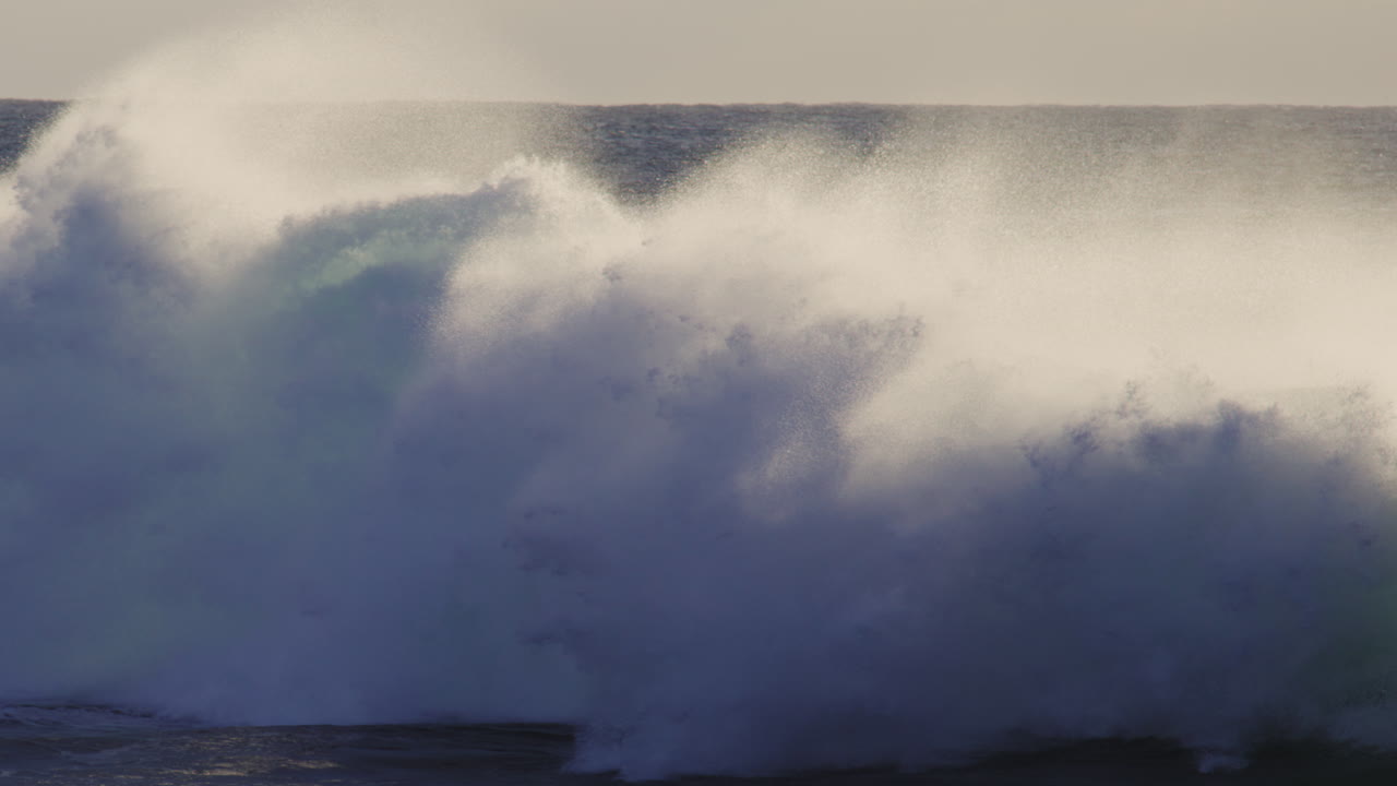 Slow motion wave breaks with mist and spray rising off top