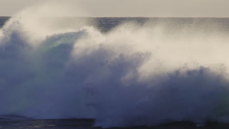 slow motion wave breaks with mist and spray rising off top