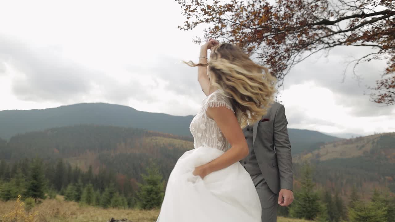 Dejlige nygifte brud og gom danser på en bjergskråning om efteråret i slow motion, bryllupspar familie