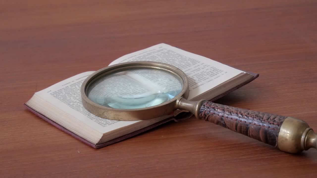 Zoom out showing an antique magnifying glass placed over the pages of an open book on a wooden table