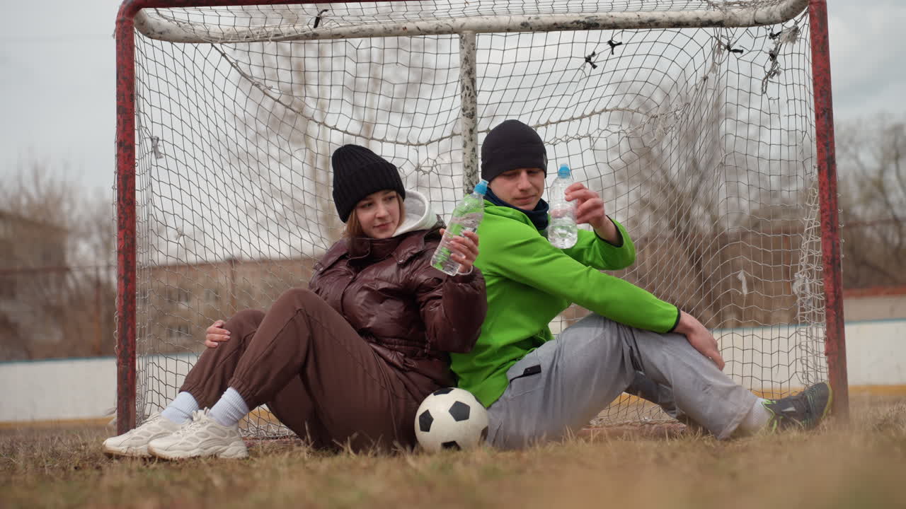 젊은 친구들이 휴식을 취하고, 십 대들이 야외에서 캐주얼 게임을 즐기며, 젊은이들이 야외에서 여가 활동을 위해 모이고, 청소년 그룹이 도시 지역의 축구장 옆에서 휴식을 취하고 있어요.