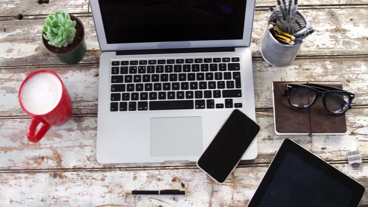 Laptop, tablet digitale, telefono cellulare e altri effetti personali su un'asse di legno.