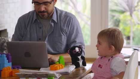 father working from home on laptop as son plays with toys