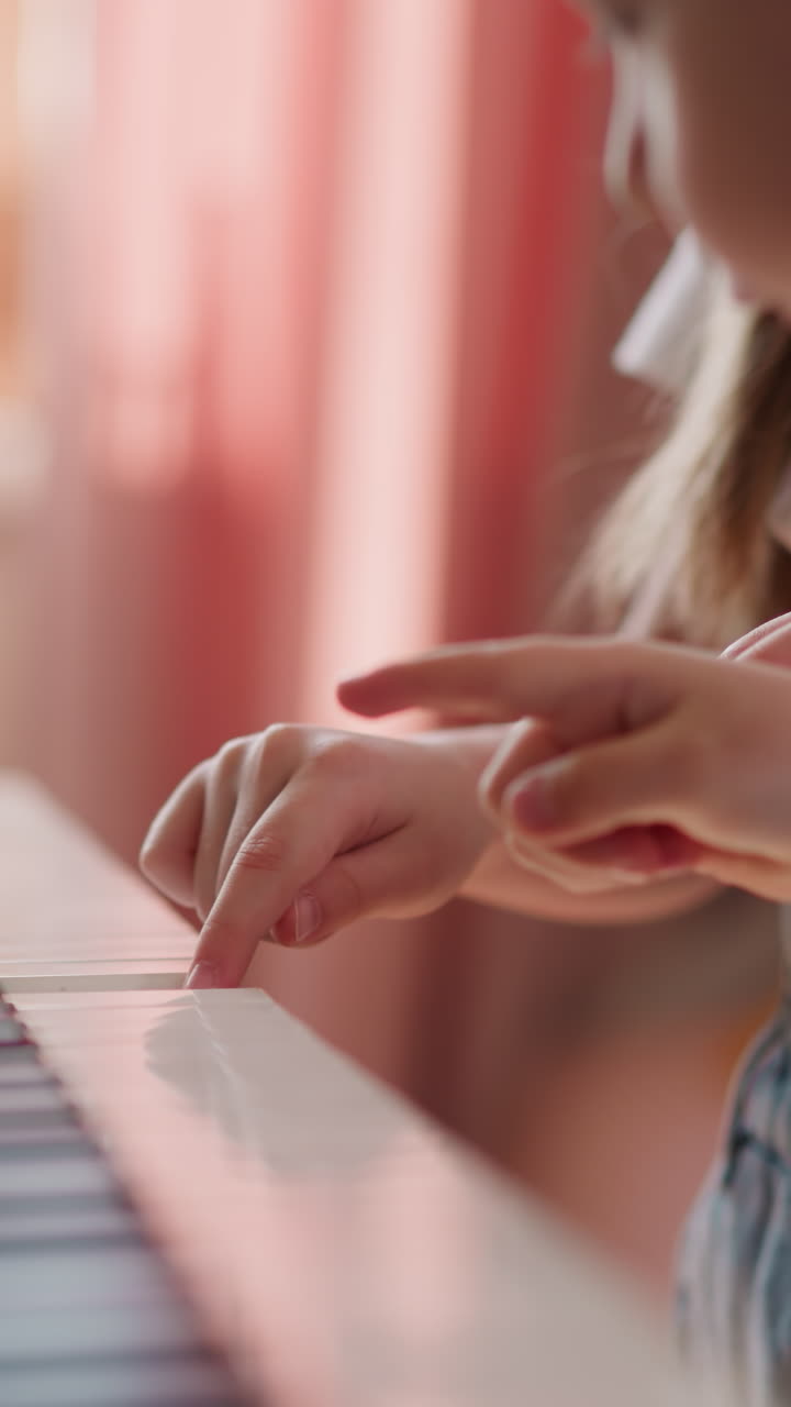 Toddler boy presses digital piano keys following elder sister at home lesson closeup. Friendly siblings learn music playing together on blurry background