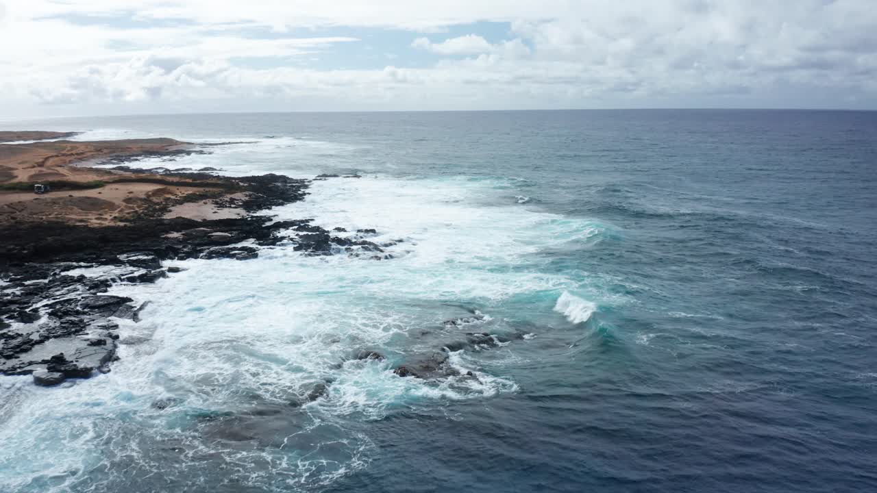 Dynamic ocean waves roll onto a rugged volcanic shoreline, creating foamy surf and dramatic contrast between land and sea on Hawaii’s southern coast