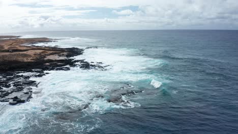 dynamic ocean waves roll onto a rugged volcanic shoreline, creating foamy surf and dramatic contrast between land and sea on hawaii’s southern coast