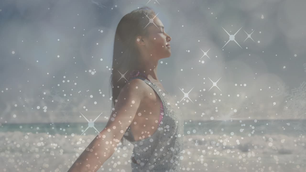 Breathing woman in gray tank top opening arms at shoreline, revealing pink swimsuit and sparkles