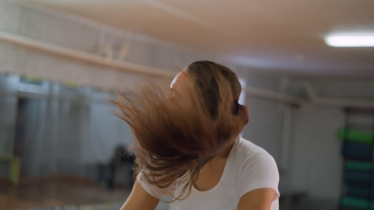 Portrait view of young girl in white top performing dance routine with strong movements flipping hair while keeping arms firm and body aligned inside studio showing strength confidence