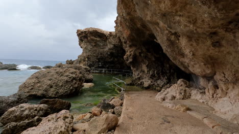 POV-shot-while-walking-on-the-rocky-coastal-path-with-sea-water-crashing-on-the-path-in-Gozo-Island,-Malta