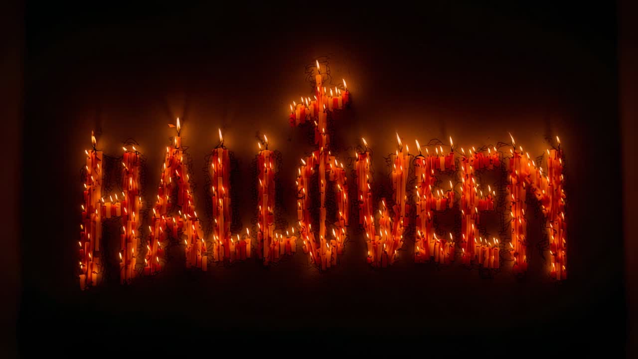 Igniting dozens of wax candles that spell HALLOWEEN in dark studio, creating pulsing orange glow