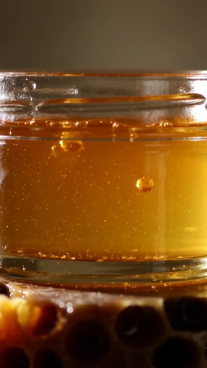 Video verticale: Barattolo di vetro su un favo che mostra gocce di miele che salgono, particelle che si sollevano per galleggiamento, cibo.