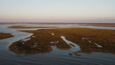 Marsh-swamp-land-of-barrier-islands-connect-to-open-ocean-at-sunset,-aerial-dolly