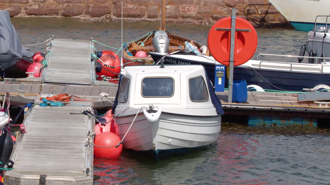 White motorboat moored at marina pontoon, gently rocking in choppy daylight coastal waters