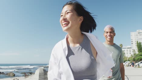 Happy-biracial-couple-walking-together-and-holding-hands-on-promenade,-in-slow-motion