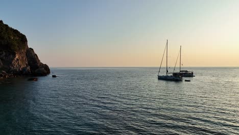 Veleros-Anclados-Cerca-De-La-Isla-De-Corfú-En-El-Mar-Jónico-Al-Atardecer,-Aguas-Tranquilas