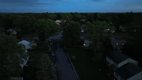 aerial revealing shot of houses and homes on dark evening in suburbia. american city suburb with single family houses in middle class housing area. wide shot. green trees in spring in the evening.