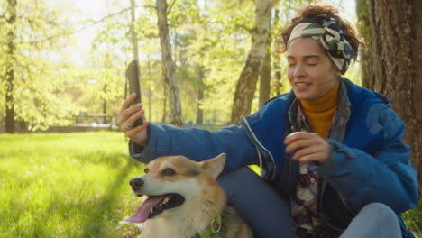woman taking selfie with corgi dog in park