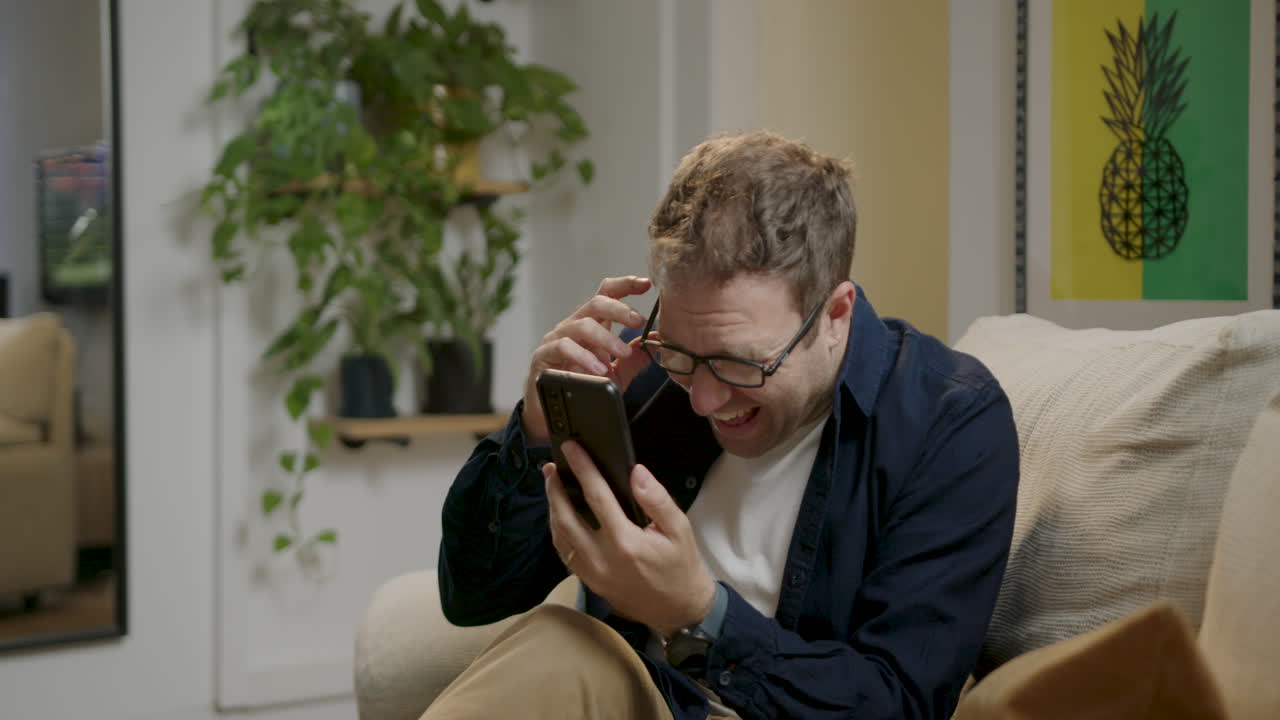 남자는 침실에서 드폰으로 보는 동안 갑자기 웃는다