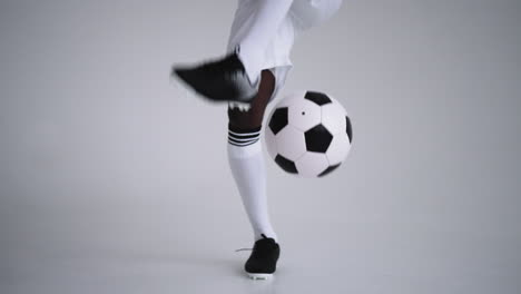 a professional black football player in a white uniform on a white background juggles a ball in slow motion. african-american ethnic group soccer player with a soccer ball