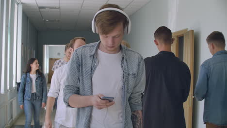 un hombre con auriculares entre la multitud de estudiantes que escuchan música está en el pasillo de la universidad durante un descanso entre clases. un introvertido en la paz interior de la universidad.