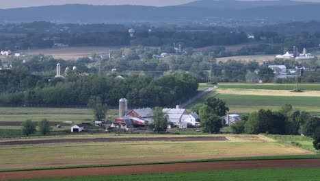 aerial zoom shot of industrial farmstead in peaceful american suburb area in spring. wide shot. forest trees and colored farm fields in rural district of town.