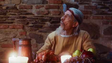 un anciano con barba de cabra come en un castillo medieval. un noble señor anciano disfruta de una comida de banquete festivo en la mesa del castillo. servicio de taberna de la época oscura