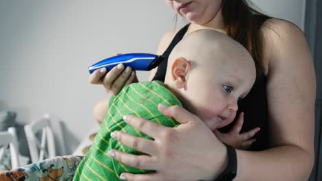 madre cortando el cabello de un hijo pequeño con un cortador de cabello en la cocina.