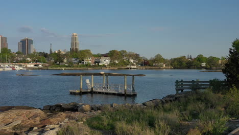 a low angle drone shot over a quiet park, heading towards calm waters with new rochelle in the background