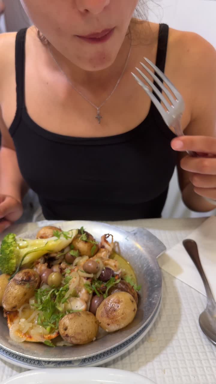 A person enjoying a traditional seafood dish with octopus, potatoes, and olives