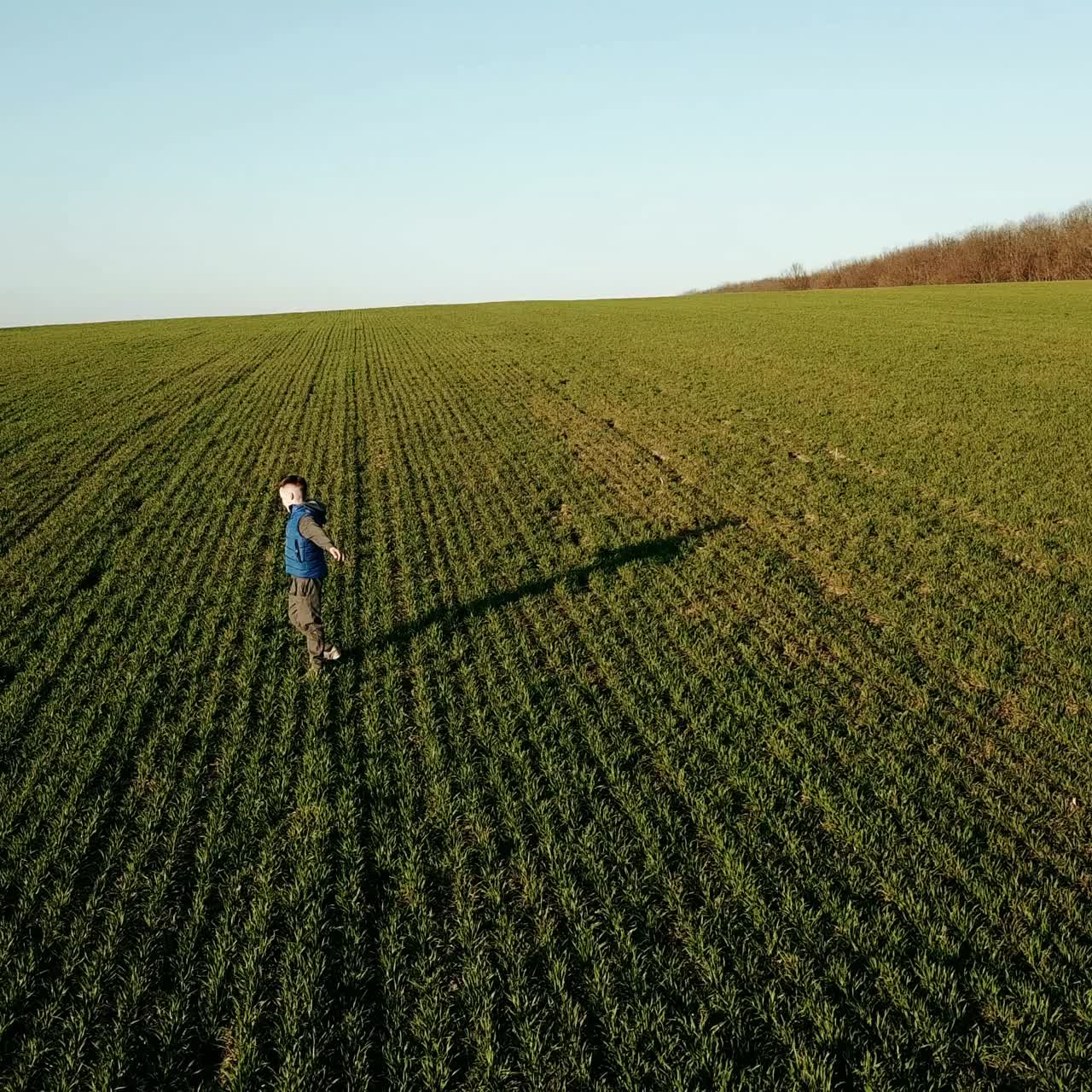 a boy in a blue vest is spinning in the middle of a field on the background of a summer landscape
