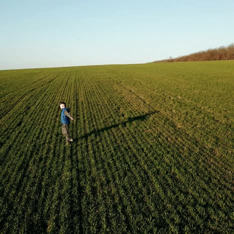 a boy in a blue vest is spinning in the middle of a field on the background of a summer landscape