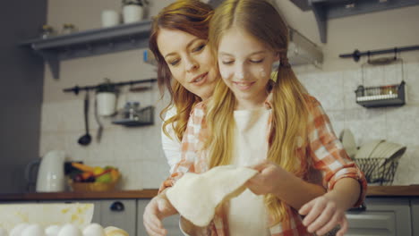 Portrait-shot-of-the-cute-teen-girl-learning-to-make-a-daugh-and-her-mother-helping-her.-cozy-nice-kitchen.-Indoors