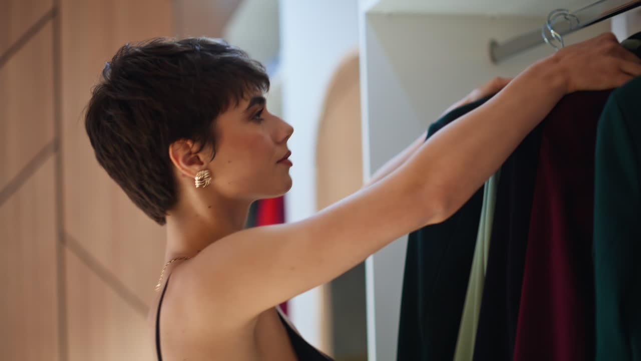 Primo piano di una donna nella cabina armadio che prende appendini ed esamina i vestiti. La donna sta selezionando un outfit.