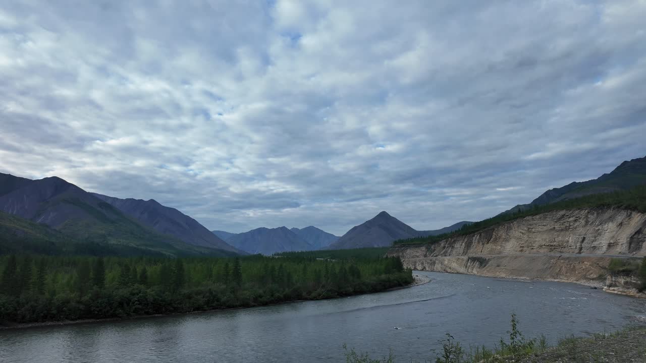조용한 강이 울창한 초록색과 웅장한 산을 가로질러 휘어지고, 황홀한 하늘 아래 구름으로 가득 차 있습니다.