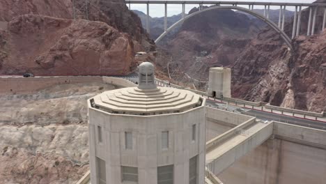 Aerial-view-of-the-Hoover-Dam-and-an-intake-tower-with-cars-doing-over-the-dam