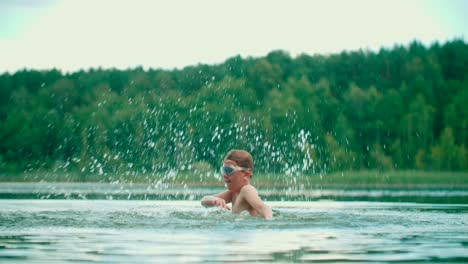 Joyful-Caucasian-kid-splashes-the-water-with-hands-and-having-fun-in-the-lake