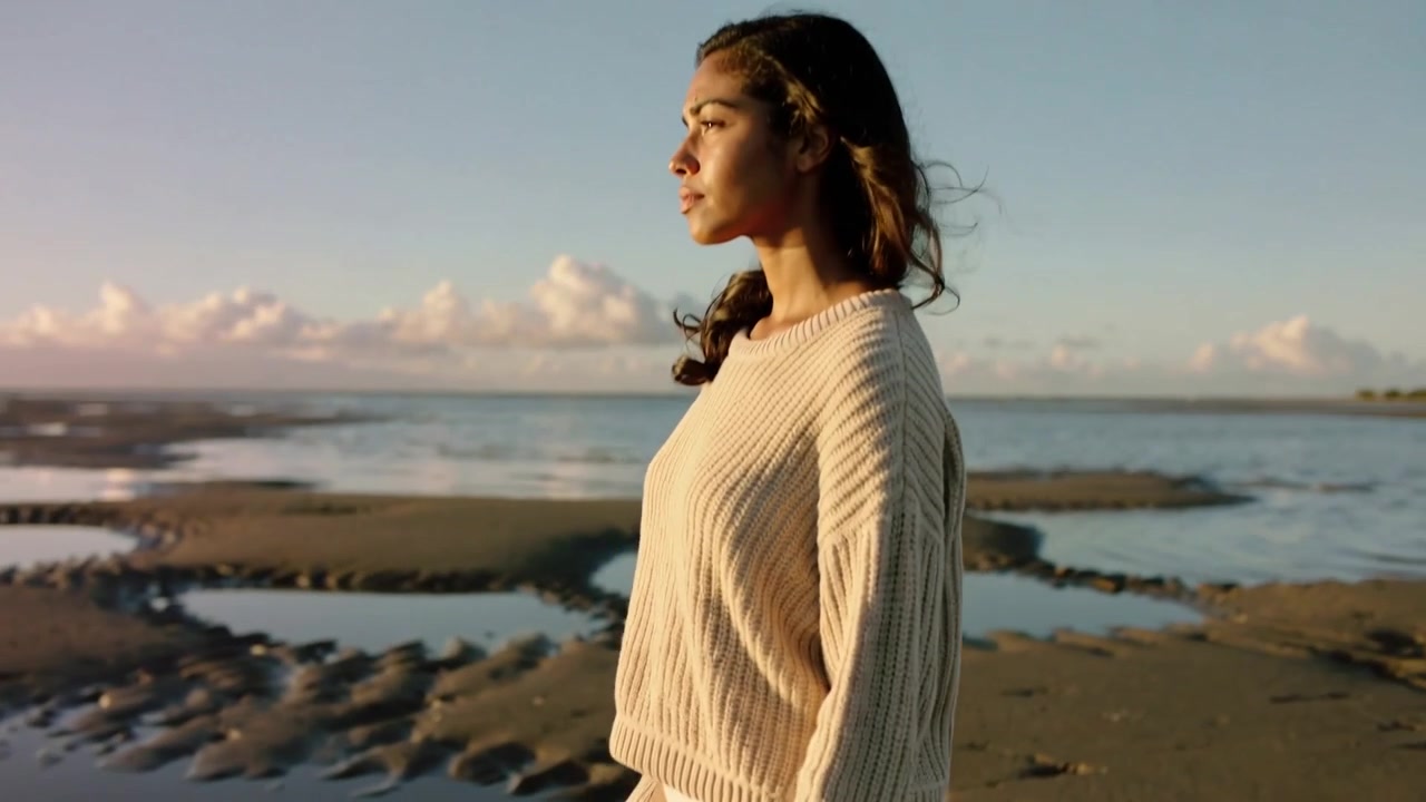 La bassa marea rivela banchi di sabbia mentre una donna cammina a piedi nudi tra le pozze di marea sulla spiaggia, indossando un maglione di maglia