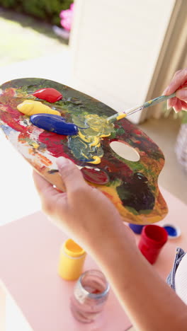 Vertical video: Mixing vibrant colors on palette, artist preparing for painting session outdoors