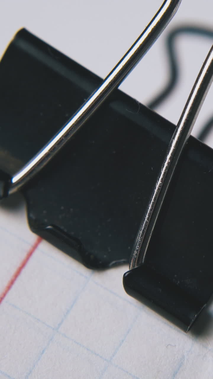 person fixes metal clamp on checkered notebook paper in white background extreme close view