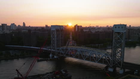 Train-on-the-Park-Avenue-Bridge,-revealing-sunset-above-Harlem,-NY---Ascending,-aerial-view