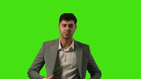 portrait of young businessman standing against green screen straightening and adjusting suit against green screen