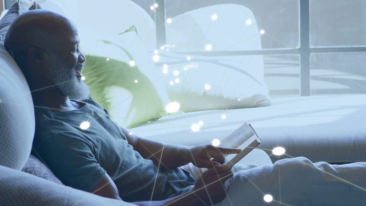 Senior man reclining on sofa, tapping tablet, reading and causing tech overlay of glowing dots
