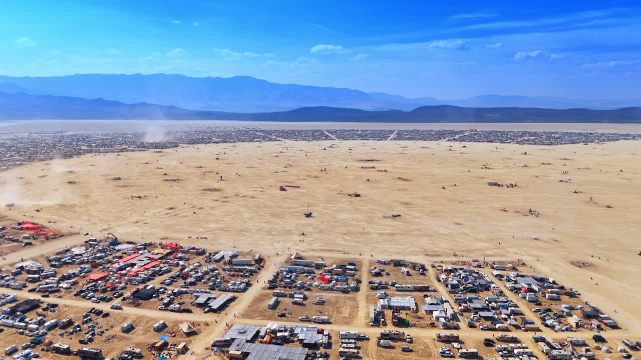 Luftaufnahme aus großer Höhe einer temporären Wüstenstadt und eines Camps. Luftbildperspektive eines riesigen Wohnmobil-Camps und eines weiten trockenen Seebeckens, umgeben von entfernten Bergen.