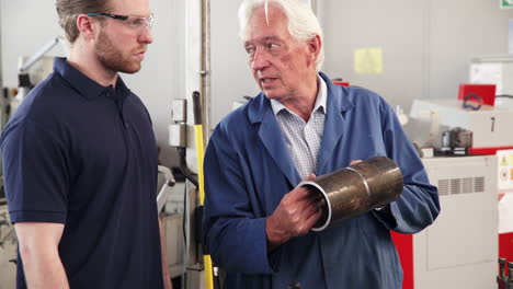 engineer teaching apprentice how to use machine in factory