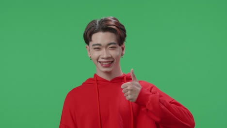 happy asian transgender male showing thumbs up gesture while standing in the green screen studio