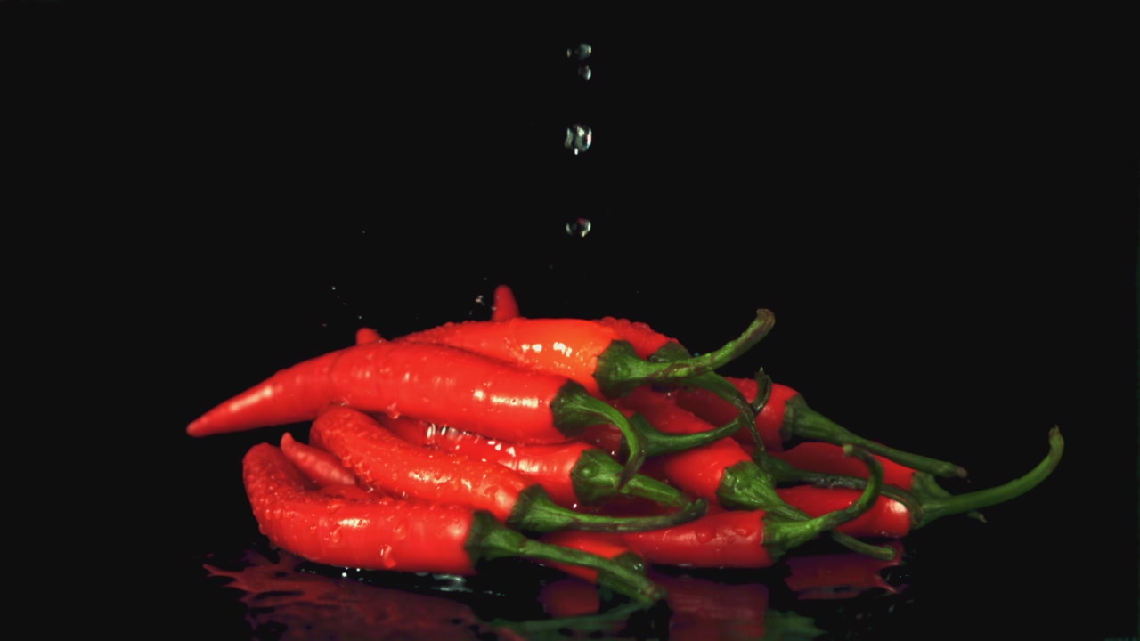 Slow Motion Water Drops Splashing on Fresh Red Chili Peppers