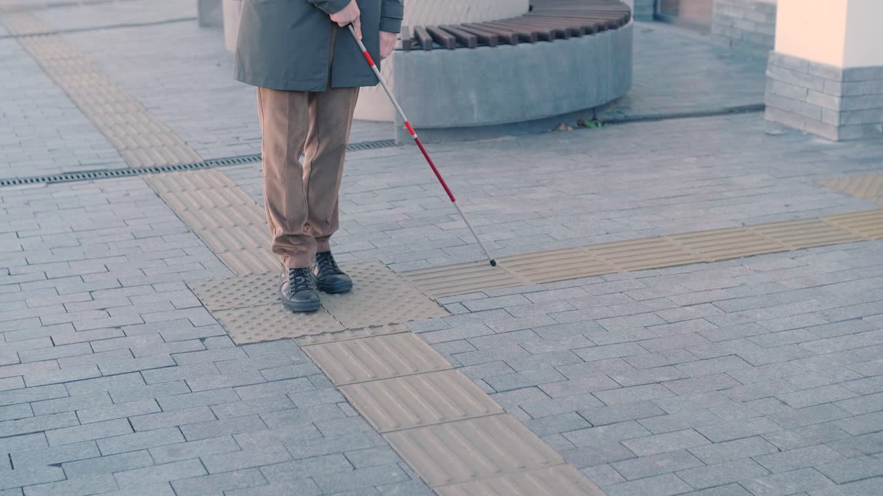 Visually impaired man is walking on a tactile warning tile with the help of his cane. Detectable warning surface for the vision impaired outdoors in the city.